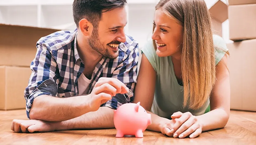 Finanças para Casais: Casal investindo em seu planejamento financeiro ao colocar uma moeda no porquinho.